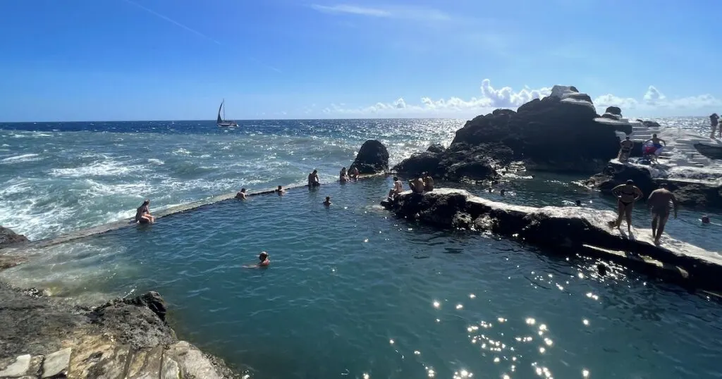 People swim and sit on the wall at the Funchal volcanic pools in Madeira.