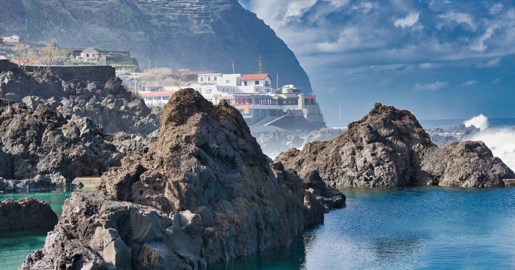 Terraced hills and Madeiran houses in the background of the Porto Moniz volcanic rockpools.