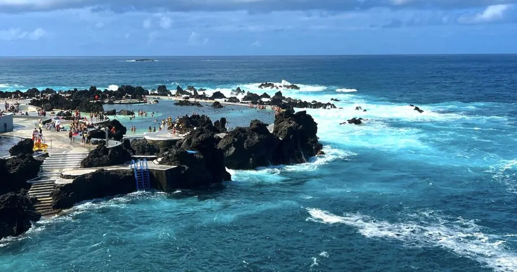 Waves roll in next to the busy Porto Moniz Natural Swimming Pools in Madeira.
