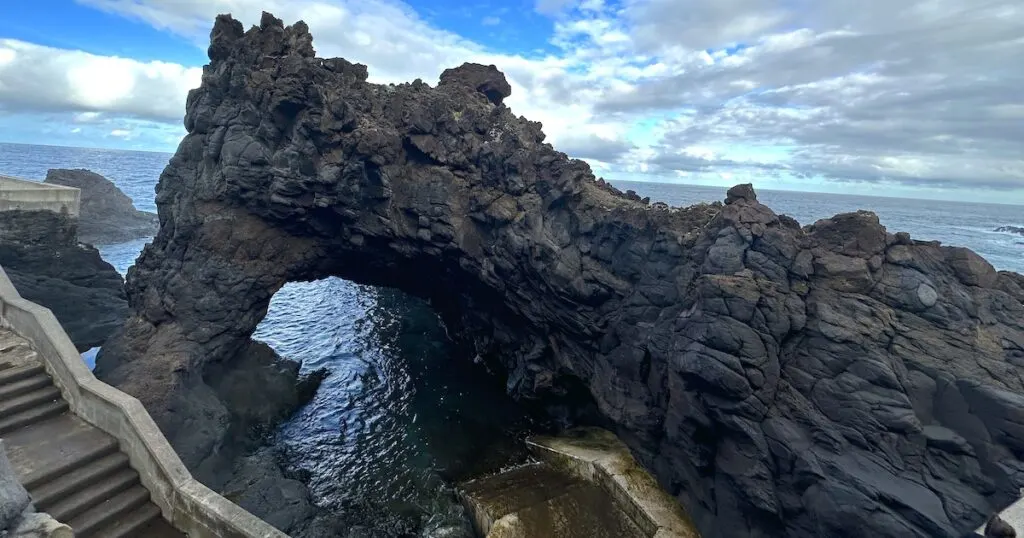 Stairs lead to a volcanic rock archway overlooking the Atlantic ocean.