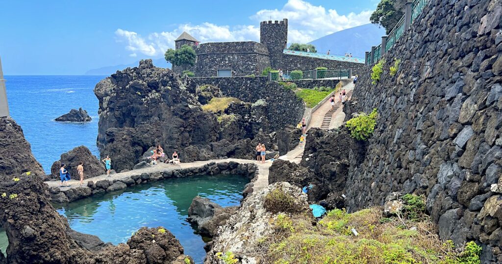 A restaurant turret extends behind a path down to natural pools in Porto Moniz.